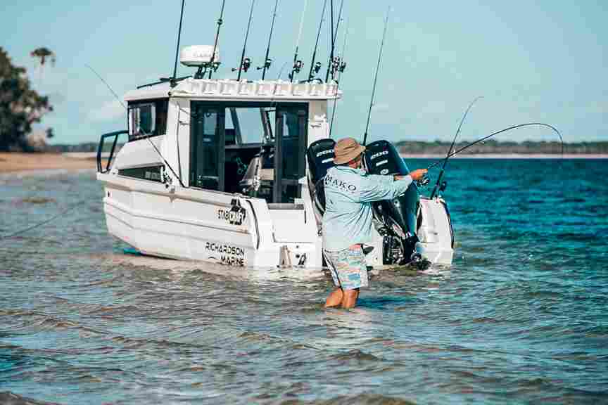 A man is fishing from his Ultracab boat in the water, surrounded by a serene natural landscape.